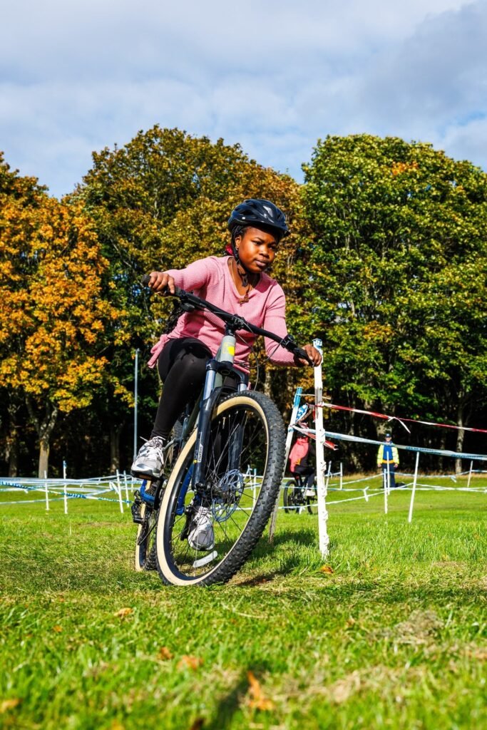 Young rider in a pink top racing past autumn trees at Inch Park